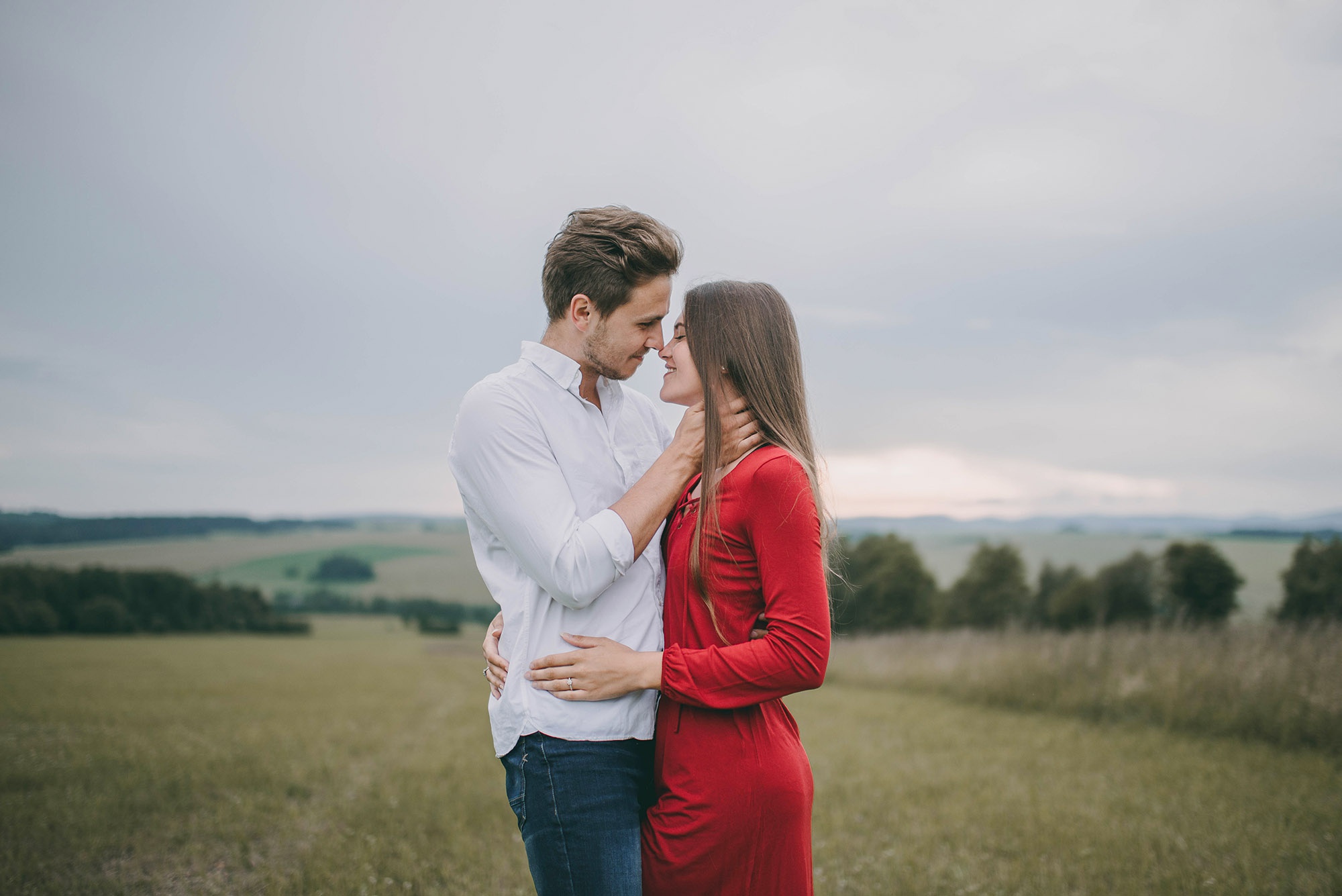 Jiri Tulach Cuddle Red Dress Brunette Field Hugging Hands On Waist Face To Face Jeans White Shirt 2000x1335