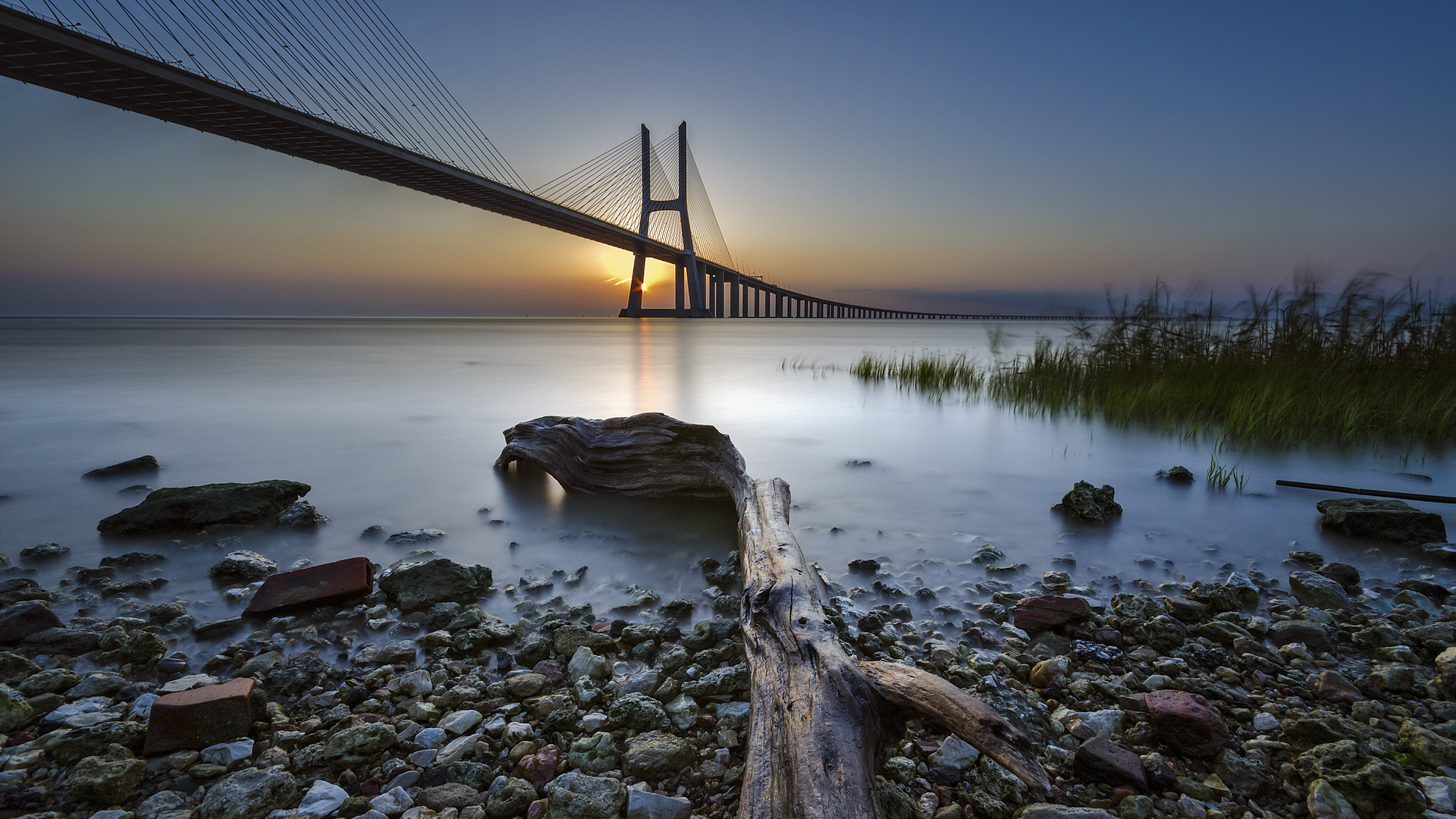 Bridge Rocks Plants Sunset Horizon Clear Sky Sun Vasco Da Gama Bridge Lisbon Portugal Architecture R 1920x1080